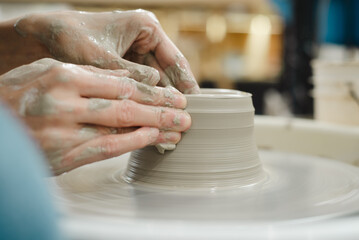 Closeup of potter hands working on pottery wheel in ceramic studio with clay hands side view