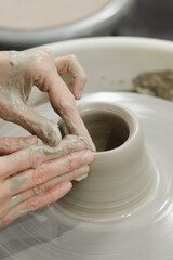 Closeup of potter hands working on pottery wheel in ceramic studio with clay hands top side view