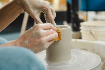 Potter hands closeup working on pottery wheel using sponge on cup in ceramic studio creating ceramic ware