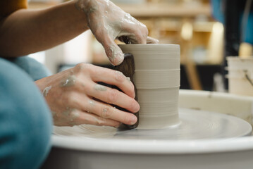 Potter hands closeup working on pottery wheel using tool to make straight edge on cup in ceramic studio creating ceramic ware