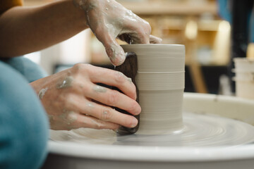 Potter hands closeup working on pottery wheel using tool to make straight edge on cup in ceramic studio creating ceramic ware
