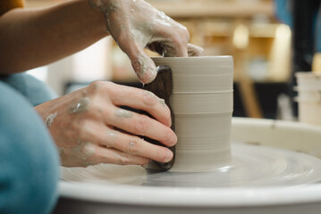 Potter hands closeup working on pottery wheel using tool to make straight edge on cup in ceramic studio creating ceramic ware