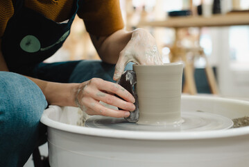 Potter hands closeup working on pottery wheel using tool to make straight edge on cup in ceramic studio creating ceramic ware