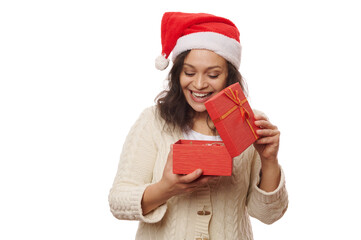 Overjoyed delightful pretty woman in Santa hat, expressing positive emotions while unpacking a cute gift box with surprise for Christmas, isolated on white background. Xmas and New Year's preparations