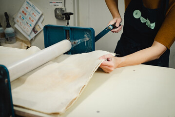 Potter working on slab roller flattening clay reading for hand building ceramic studio workshop