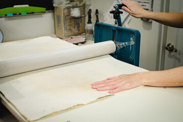 Potter working on slab roller flattening clay reading for hand building ceramic studio workshop