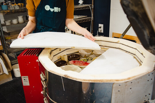 Potter unloading ceramic kiln in studio. Hands and pottery. Large kiln trays.