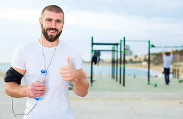 Athletic man is standing on a modern sports ground near the sea shore.