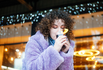 smiling woman drinks mulled wine outdoors, festive background
