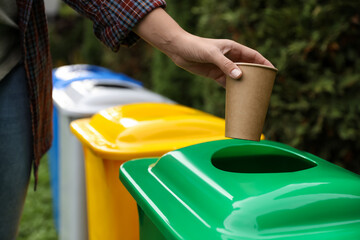 Woman throwing coffee cup into recycling bin outdoors, closeup