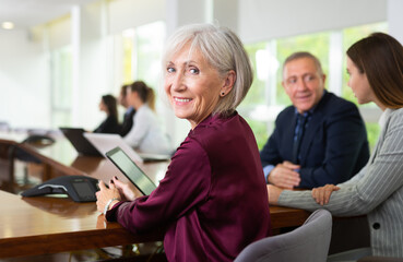 Side view portrait of friendly smiling classy gray-haired senior white businesswoman sitting at table during corporate team meeting in conference room  - obrazy, fototapety, plakaty