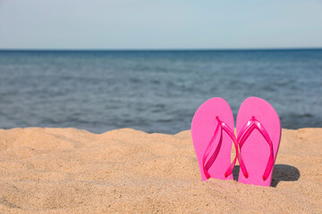 Fototapeta na wymiar Stylish pink slippers on sand near sea, space for text. Beach accessory