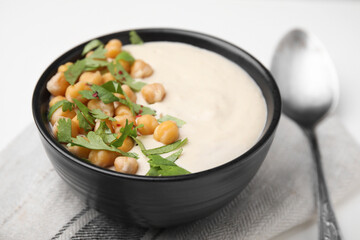 Tasty chickpea soup in bowl, spoon and napkin on white table, closeup
