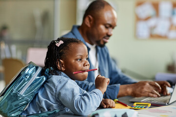 Side view portrait of cute black girl playing with pencils while father working in background
