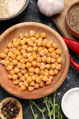 Delicious chickpeas and different products on black textured table, flat lay. Hummus ingredient