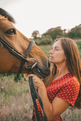 Obraz premium portrait of a beautiful long-haired girl in a red dress and a horse in a grove,