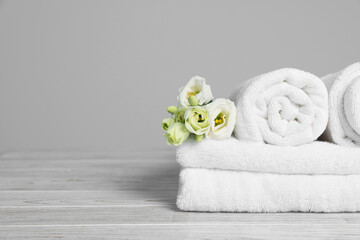 Obraz na płótnie Canvas Soft white towels with flowers on wooden table against grey background, space for text