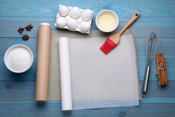 Rolls of baking parchment paper, different ingredients and kitchen tools on light blue wooden table, flat lay. Space for text