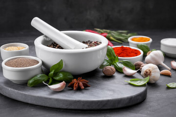 Mortar with pestle and different spices on black table, space for text