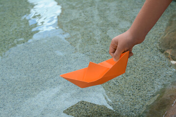 Fototapeta na wymiar Kid launching small orange paper boat on water outdoors, closeup