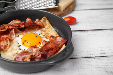 Delicious crepe with egg and bacon in dish on white wooden table. Breton galette