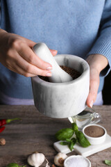 Woman grinding coriander at wooden table, closeup