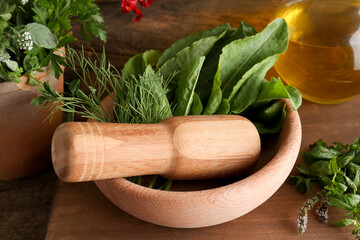Mortar with pestle, fresh green herbs and oil on wooden table