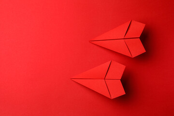 Handmade paper planes on red background, flat lay. Space for text