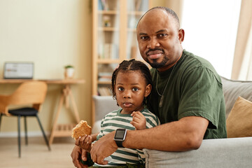 Cozy portrait of black father and daughter looking at camera in home setting, copy space