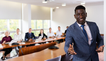 Portrait of positive african-american man in suit offering a handhsake and looking at camera. Friendly businessman in meeting room.