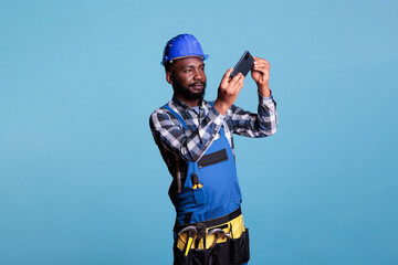 African american construction worker taking picture with mobile phone isolated on blue background...