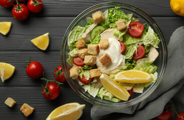 Bowl of delicious salad with Chinese cabbage, lemon, tomatoes and bread croutons on black wooden table, flat lay