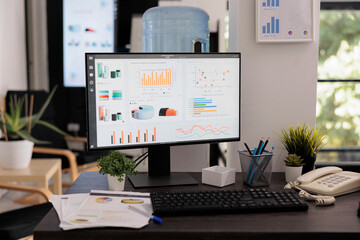 Close up view of monitor with sales growth graphs on screen previous to brainstorming meeting. Placed on desk statistical reports printed on handouts and work materials.