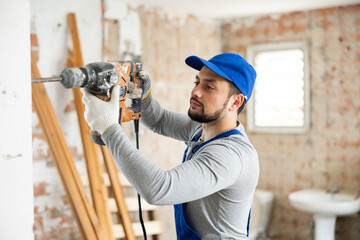 Portrait of skilled maintenance worker holding hammer drill perforator standing at indoor building...