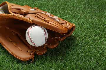Catcher's mitt and baseball ball on green grass, space for text. Sports game