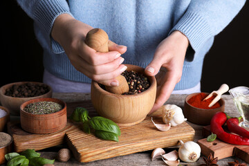 Woman grinding peppercorns at wooden table, closeup