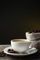 Cup of hot aromatic coffee and roasted beans on wooden table against dark background