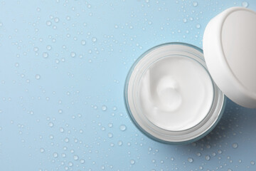 Jar of face cream on light blue surface covered with water drops, flat lay. Space for text