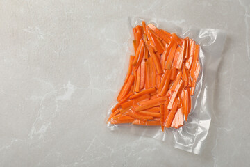 Vacuum packing with cut carrots on light grey marble table, top view. Space for text