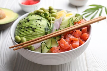 Delicious poke bowl with avocado, fish and edamame beans on white wooden table, closeup