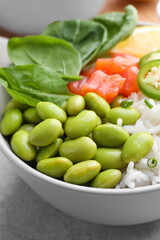 Poke bowl with salmon, edamame beans and rice on light grey table, closeup