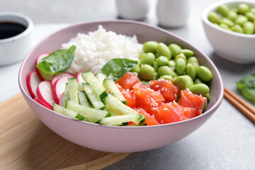 Poke bowl with salmon, edamame beans and vegetables on light grey table