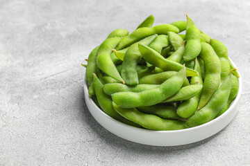 Plate with green edamame beans in pods on light grey table. Space for text