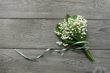 Tuinposter Lily of the valley flowers  on  wooden rustic background. Beautiful bouquet of white flowers with green leaves. Top view, free space, card for women's day, mother's day © Leka