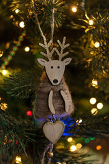 Christmas wooden deer, handmade, on the background of a Christmas tree decorated with lights of garlands