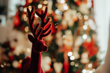 Red velvet reindeer Christmas decoration close up with Christmas tree blurred background