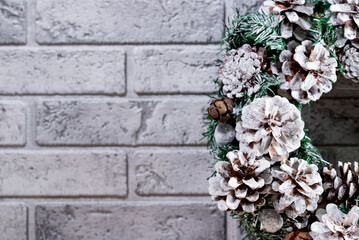 Fototapeta na wymiar Christmas wreath made of fir branches and natural cones. Against the background of a gray brick wall. New Year and winter holidays. Christmas decor. Close-up, free space for your text