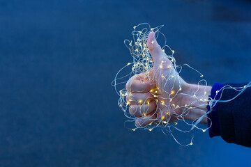 Thumb up in Christmas lights. Man showing thumbs on the blue background. New Year and Christmas concept background.