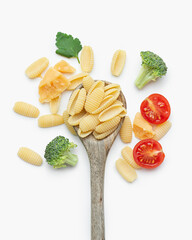 Raw pasta with tomatoes, broccoli, parsley and parmesan in a wooden spoon on a white background