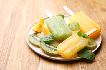 Plate of tasty orange and kiwi ice pops on wooden table. Fruit popsicle